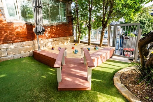 Outdoor sandpit play area with wooden bridge and toys at Balmain Road Montessori childcare centre