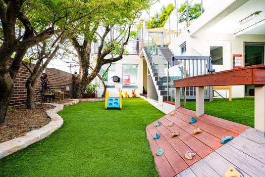 Outdoor Montessori play area with climbing ramp and trees at Balmain Road childcare centre