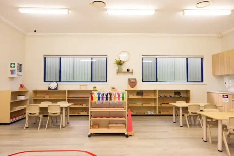 Montessori classroom at Mount Annan childcare with central learning shelf, wooden tables and organised activity areas