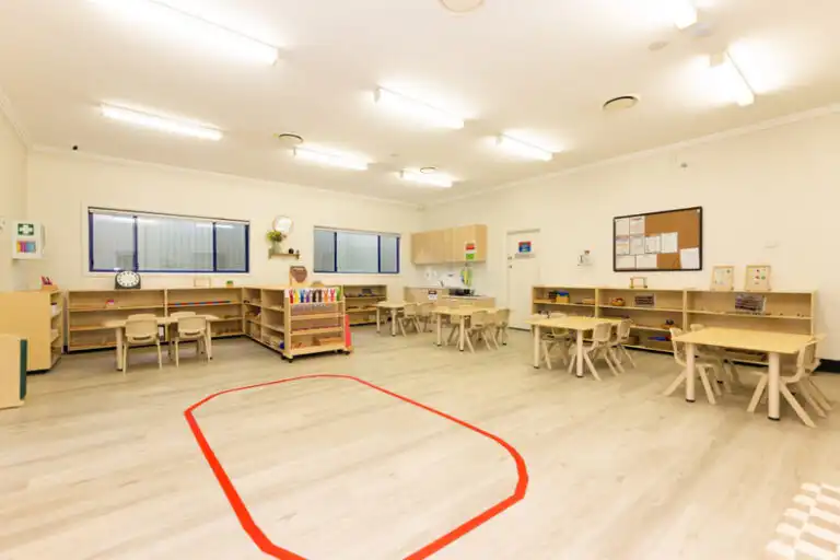 Large Montessori classroom at Mount Annan childcare centre with open floor space, wooden tables and learning shelves