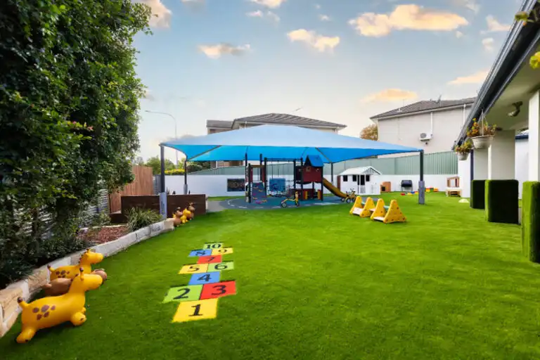 Outdoor play area at Mount Annan Montessori childcare with shaded playground, artificial grass and hopscotch markings