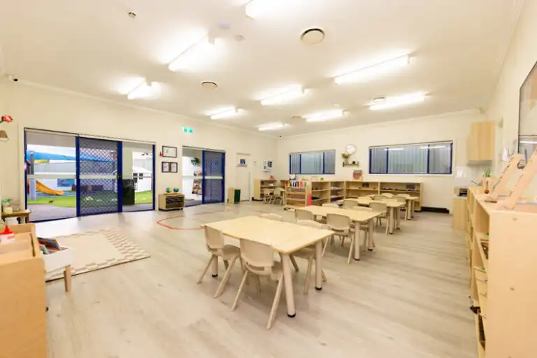 Bright Montessori classroom at Mount Annan childcare with wooden tables, open shelving and outdoor access