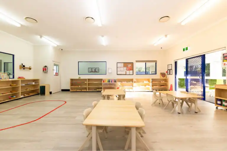 Bright Montessori classroom at Mount Annan childcare with wooden tables, open shelving and outdoor access