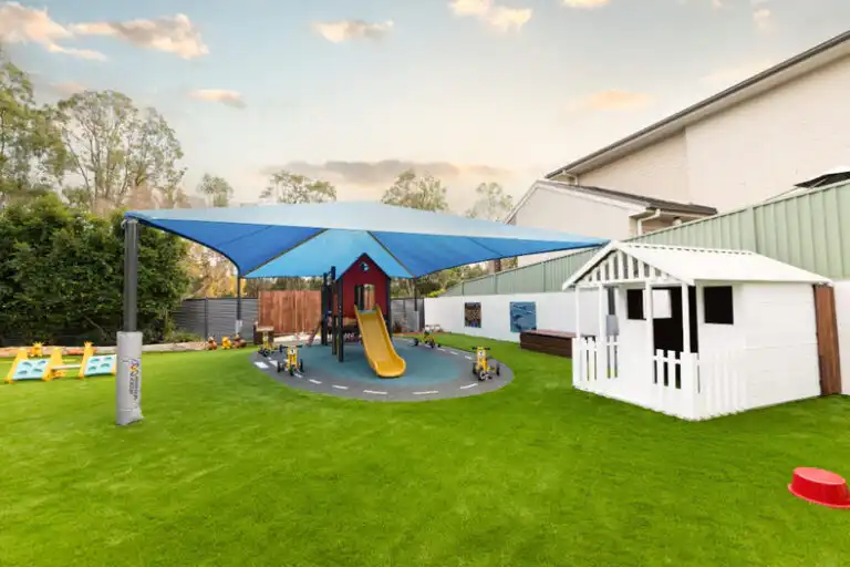 Outdoor Montessori play area at Mount Annan childcare with shaded playground, slide, playhouse and artificial grass