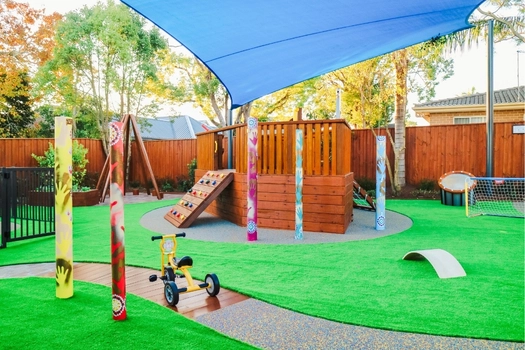 Shaded outdoor playground at Revesby Montessori Academy with climbing equipment and tricycle