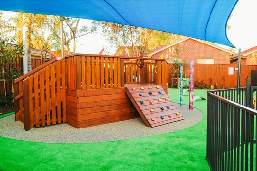 Outdoor playground at Revesby Montessori Academy with wooden climbing structure and shaded play space