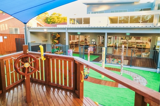 Outdoor playground at Revesby Montessori Academy with wooden play structure and centre building view