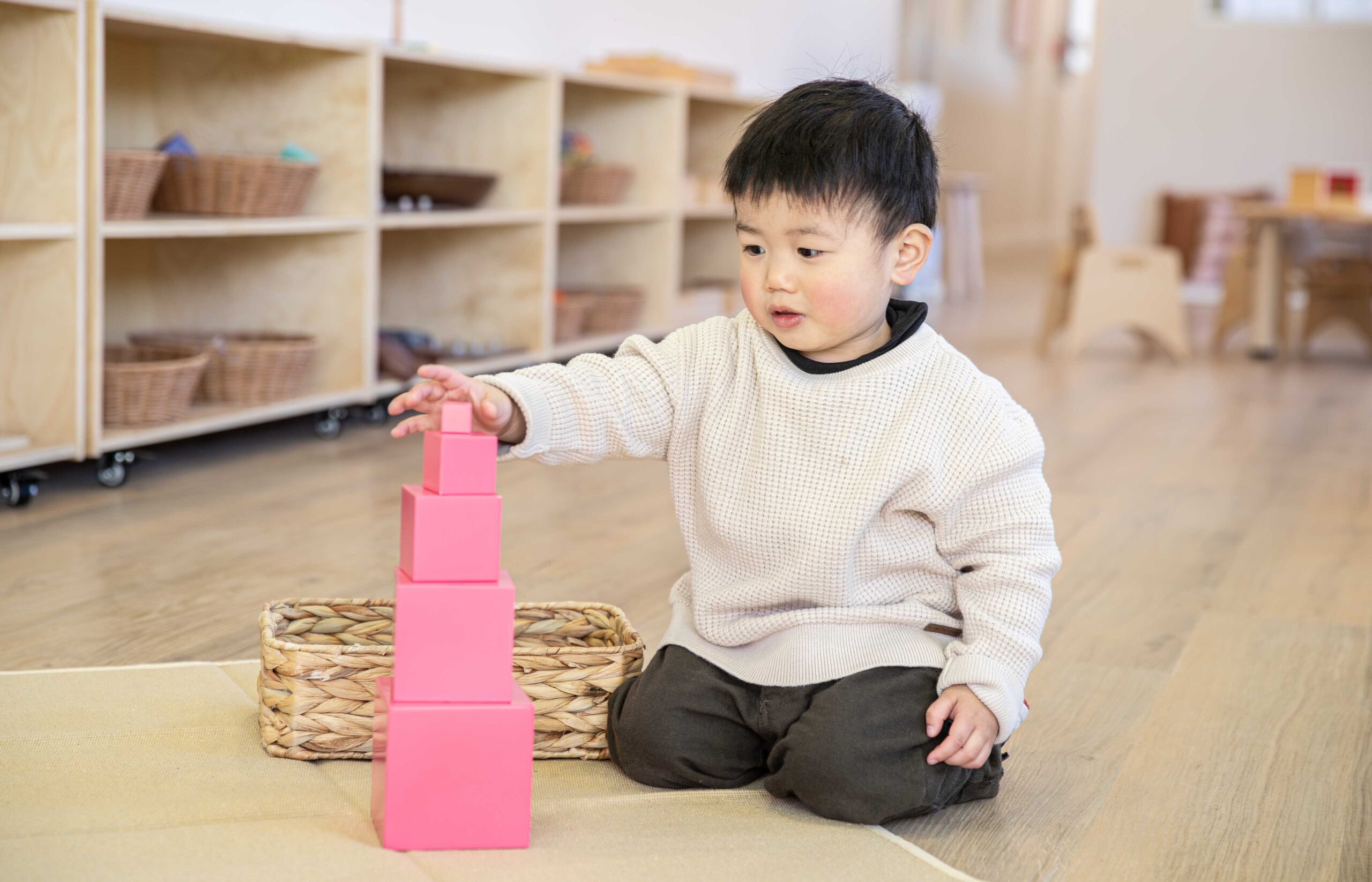 Child building a Montessori Pink Tower, placing the smallest pink cube on top of the stacked cubes in a Montessori classroom