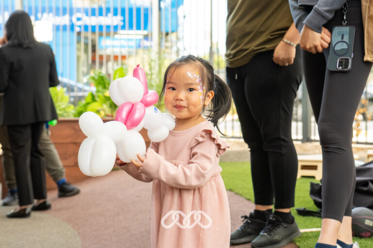 Young child holding a colourful balloon creation at the Heidelberg West Montessori Academy Grand Opening.